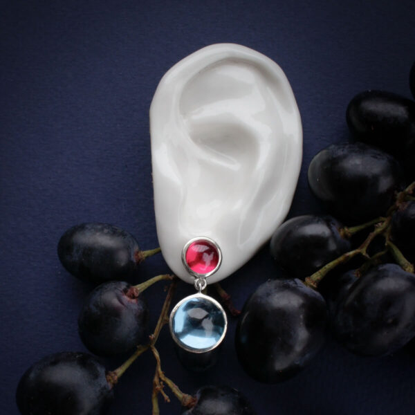 Hõbedast kõrvarõngas rubiinpunase ja sinise kiviga kõrvas, tumedal taustal