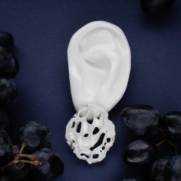 hõbedast orgaanilise avatud mustriga kõrvarõngas kõrvas, kaasaegne käsitööehe tumedal taustal