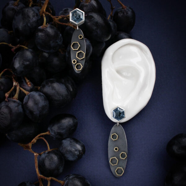 „Stellar” kõrvarõngad hõbedast ja messingist sinise kuusnurkse kiviga, viinamarjade ja kõrva maketi taustal