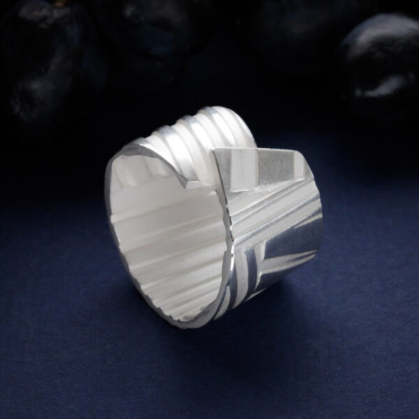 hõbedast triibuline sõrmus arhitektuurse geomeetrilise vormiga tumedal taustal