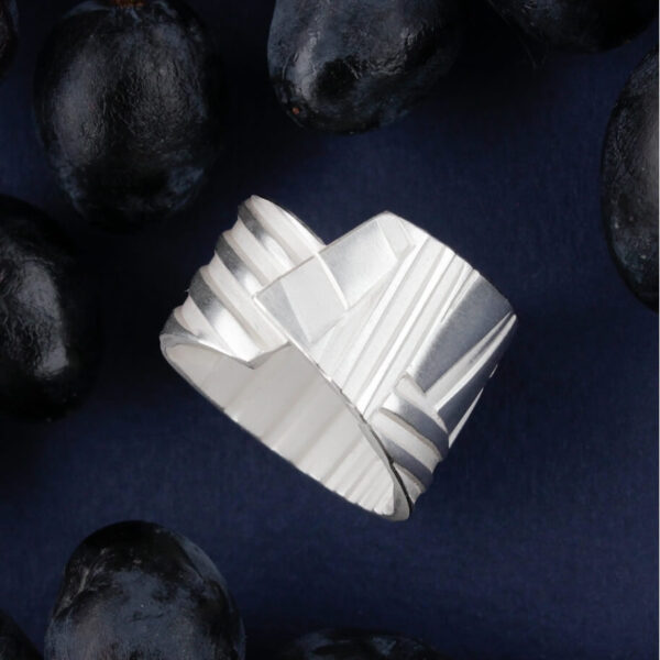 hõbedast triibuline sõrmus skulpturaalse geomeetrilise disainiga tumedal taustal