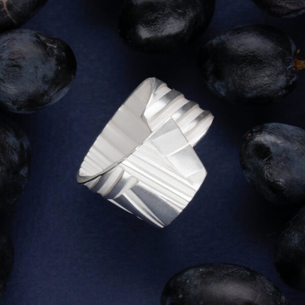 hõbedast triibuline sõrmus geomeetrilise disainiga tumedal taustal