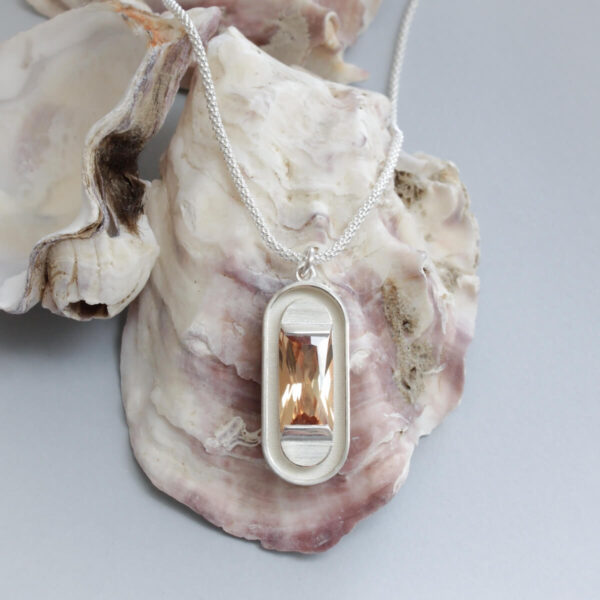 Hõbedast kaelakee ristkülikukujulise ripatsiga, mille keskmes on hele šampanja toonis kivi. Esitletud elegantses mustas ehtekarbis, sobides ideaalselt kingituseks. Minimalistlik disain ja pehme värvigamma loovad ajatu ehte, mis täiendab nii igapäevast kui pidulikku stiili. Käsitööna valminud disainehe Eesti ehtekunstnikult Katrin Veegenilt.